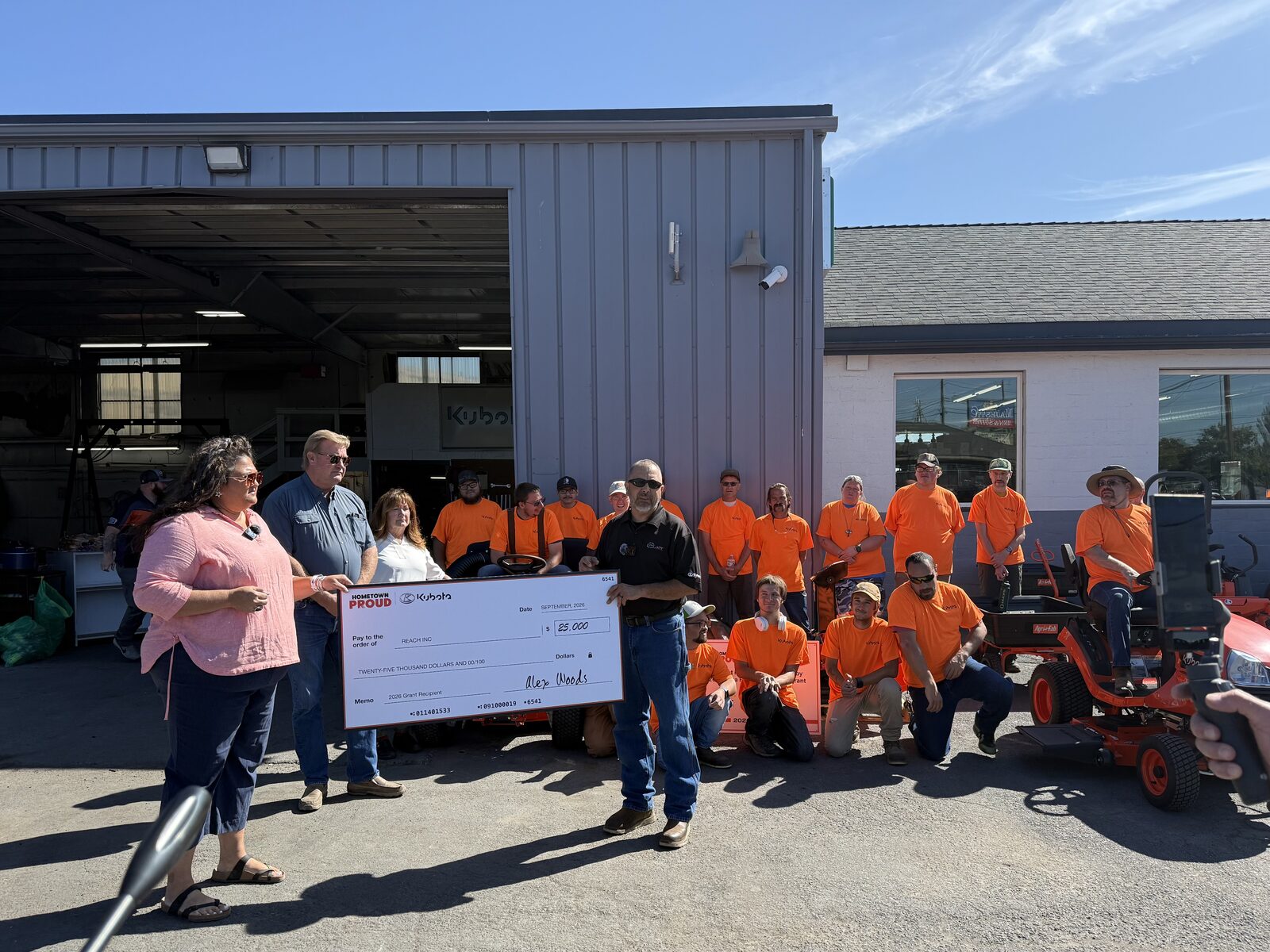 REACH, Inc. accepts the $25,000 cash half of its Kubota Hometown Proud grant, with the Ready Set Mow crew behind, at Pelican Tractor on South 6th Street in Klamath Falls, Tuesday, September 15, 2026.