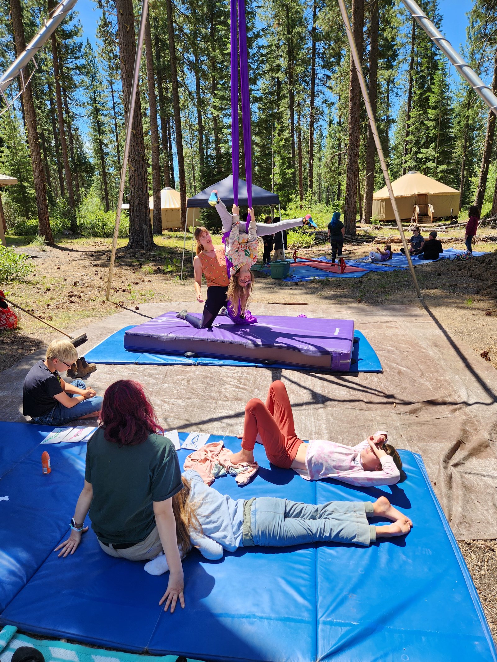 A camper having a great time doing an upside-down trick on aerial silks
