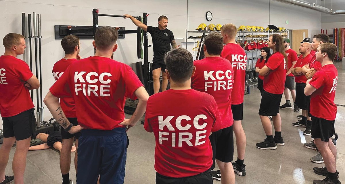 KCC Fire students gather around an instructor in a training facility during a physical training session