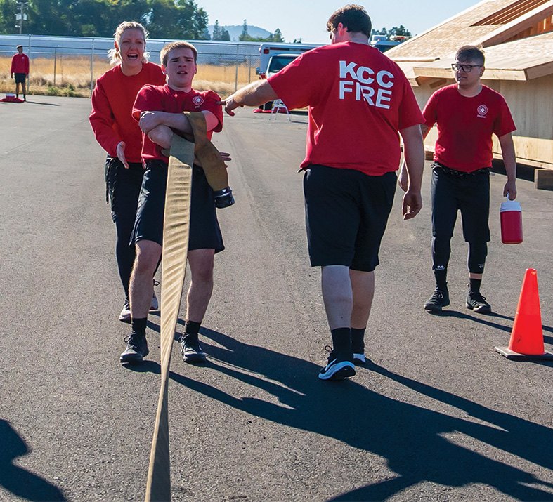 KCC Fire students carry a rolled fire hose during an outdoor physical training drill
