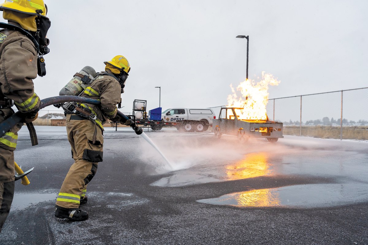 Firefighting students in full turnout gear extinguish a live vehicle fire during a KCC training exercise