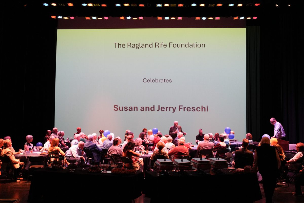 Wide view of the reception tables on the Ross Ragland Theater stage under a screen reading The Ragland Rife Foundation Celebrates Susan and Jerry Freschi