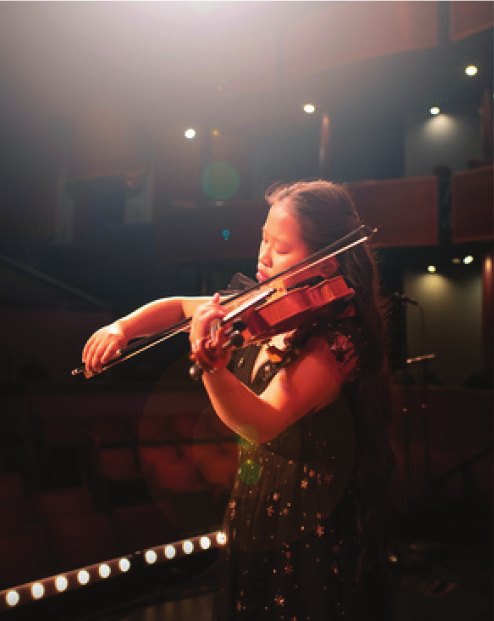 A violinist plays on stage at the Ross Ragland Theater, lit from above