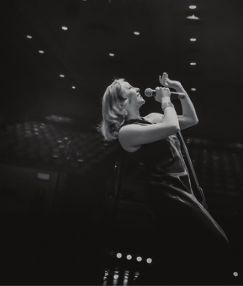 Black-and-white photo of a vocalist singing into a handheld microphone on a darkened stage