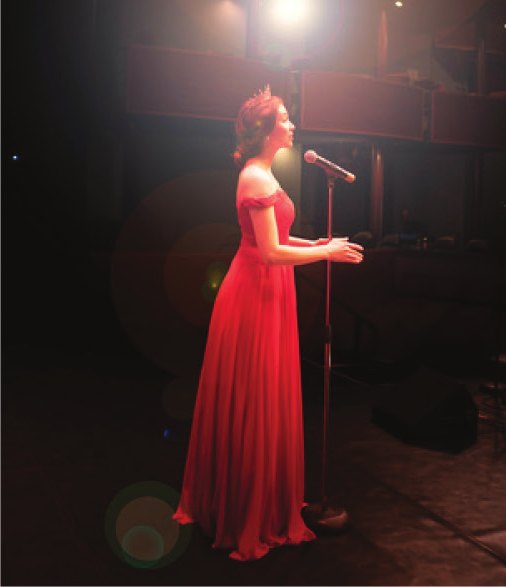 A soloist in a red gown sings at a microphone stand on the Ross Ragland Theater stage