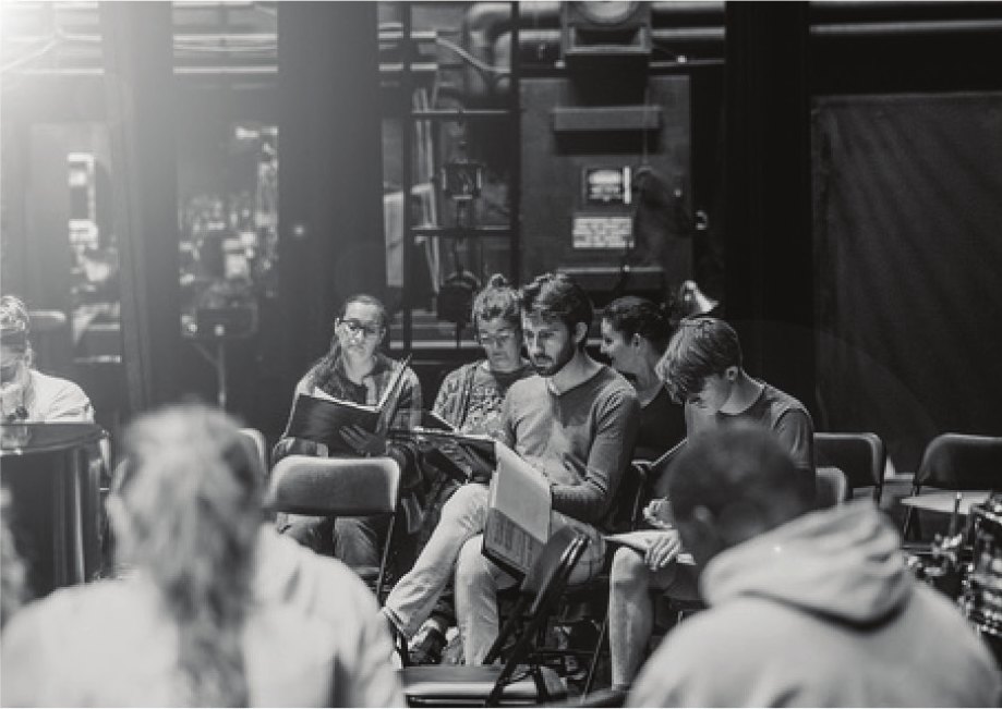Black-and-white photo of musicians rehearsing with sheet music in the theater seats