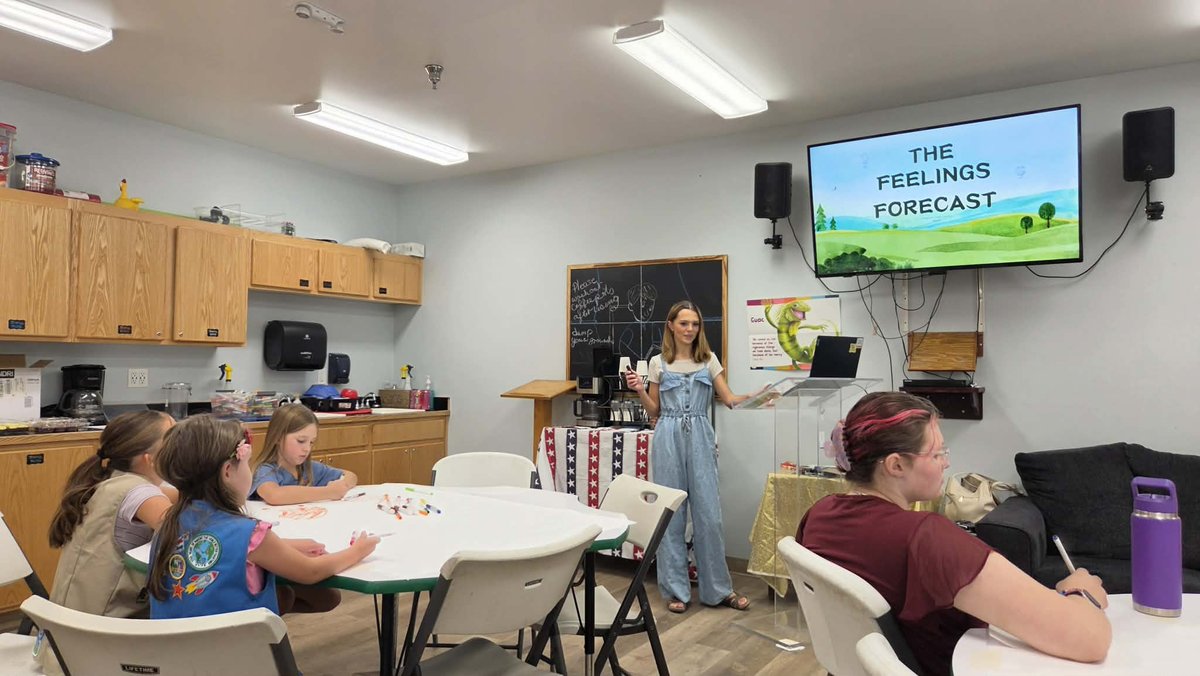 Tenaya Cherrick presenting The Feelings Forecast to a room of Girl Scouts and parents, the slide on the screen behind her