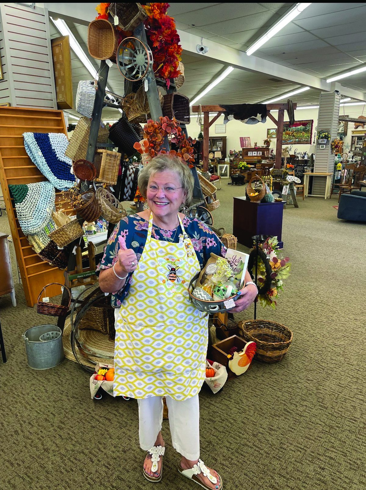 Woman in a yellow apron standing among autumn décor and vintage finds at Honey & Ivy Collective