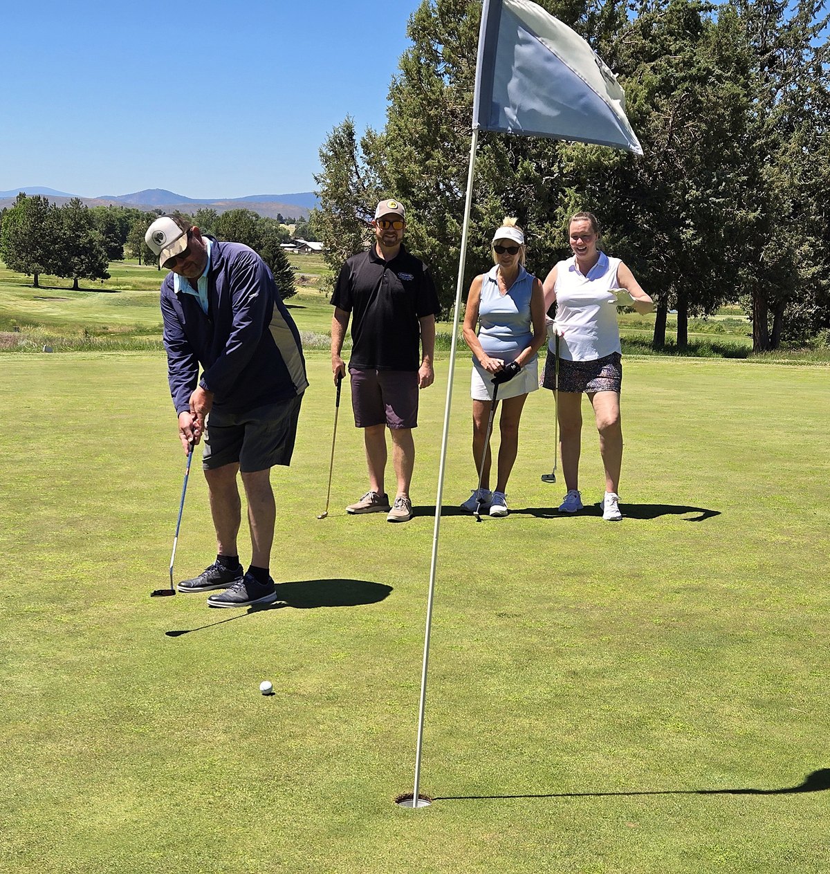 A team lines up a putt on the green beside the flagstick at Shield Crest Golf Club